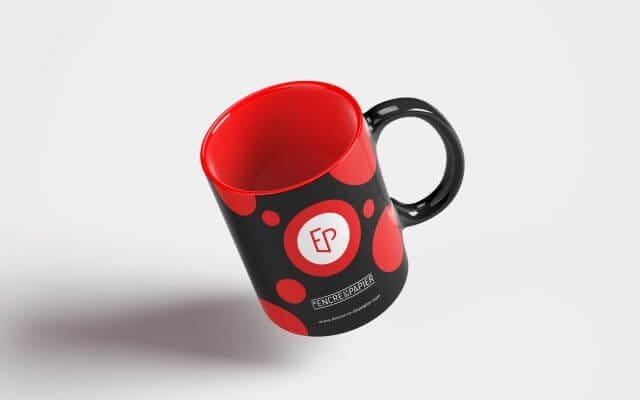 un mug en lévitation sur un fond gris clair. Ce mug noir à pois rouge sur les faces a une anse noire et un fond rouge. Le logo de l'encre et du papier est apposé en blanc avec également le nom de l'entreprise et l'adresse du site web