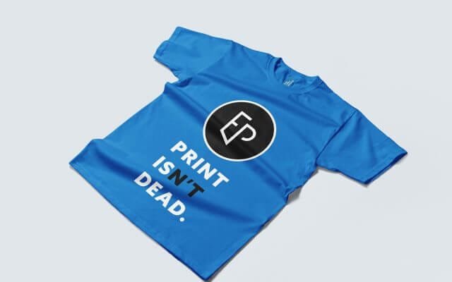 Un tee-shirt bleu roi posé sur un fond gris clair avec le logo de De l'Encre & du Papier et le slogan Print isn't dead en dessous.