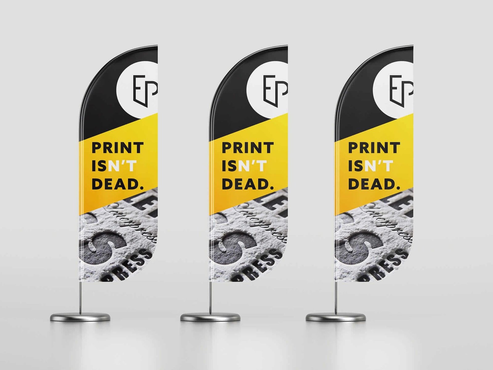 Un exemple de PLV : trois drapeaux alignés sur fond gris représentant un visuel qui contient le logo De l'Encre & du Papier et le slogan Print Isn't Dead